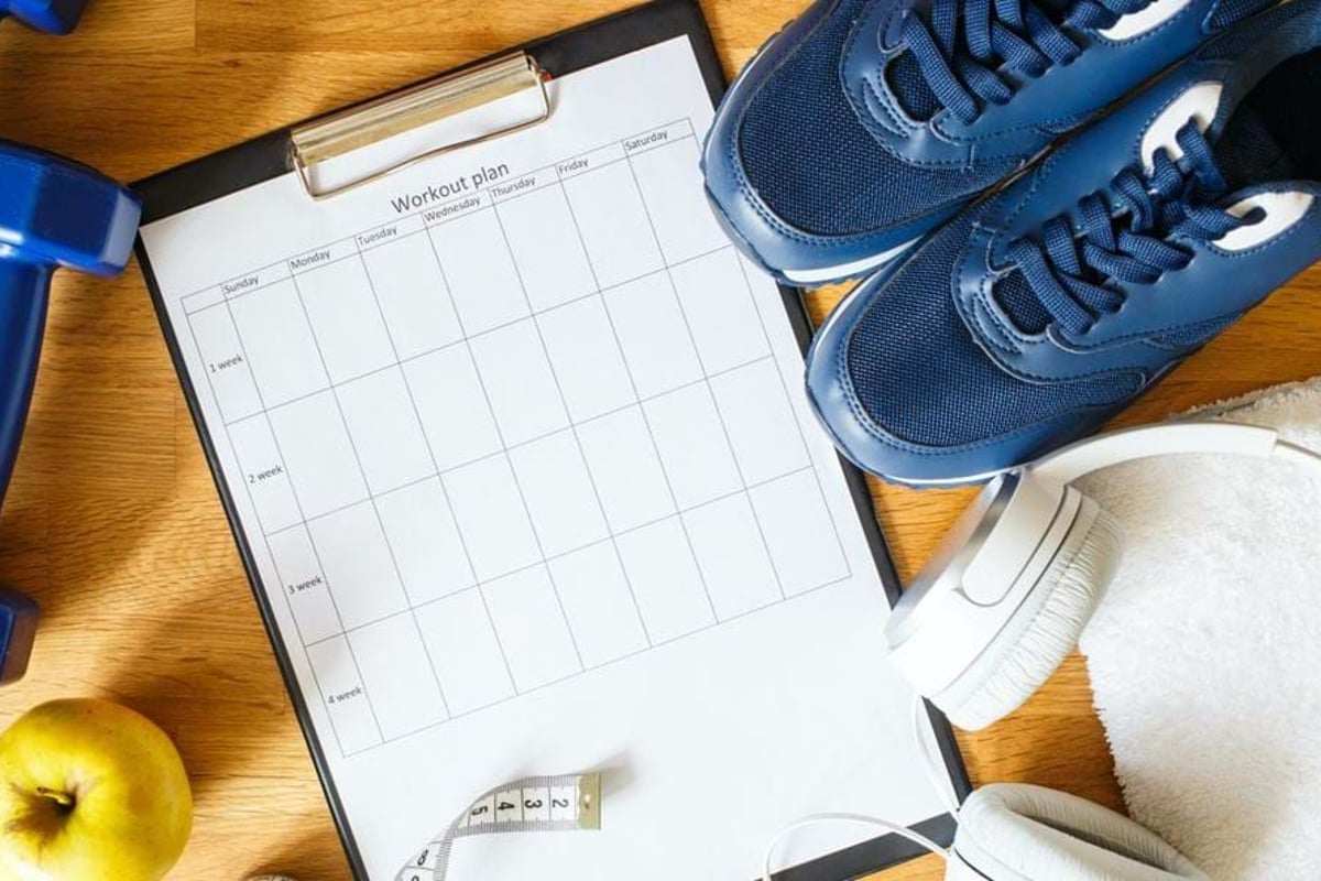 Workout plan sheet with blue trainers, dumbbell, apple, headphones, and towel on wood