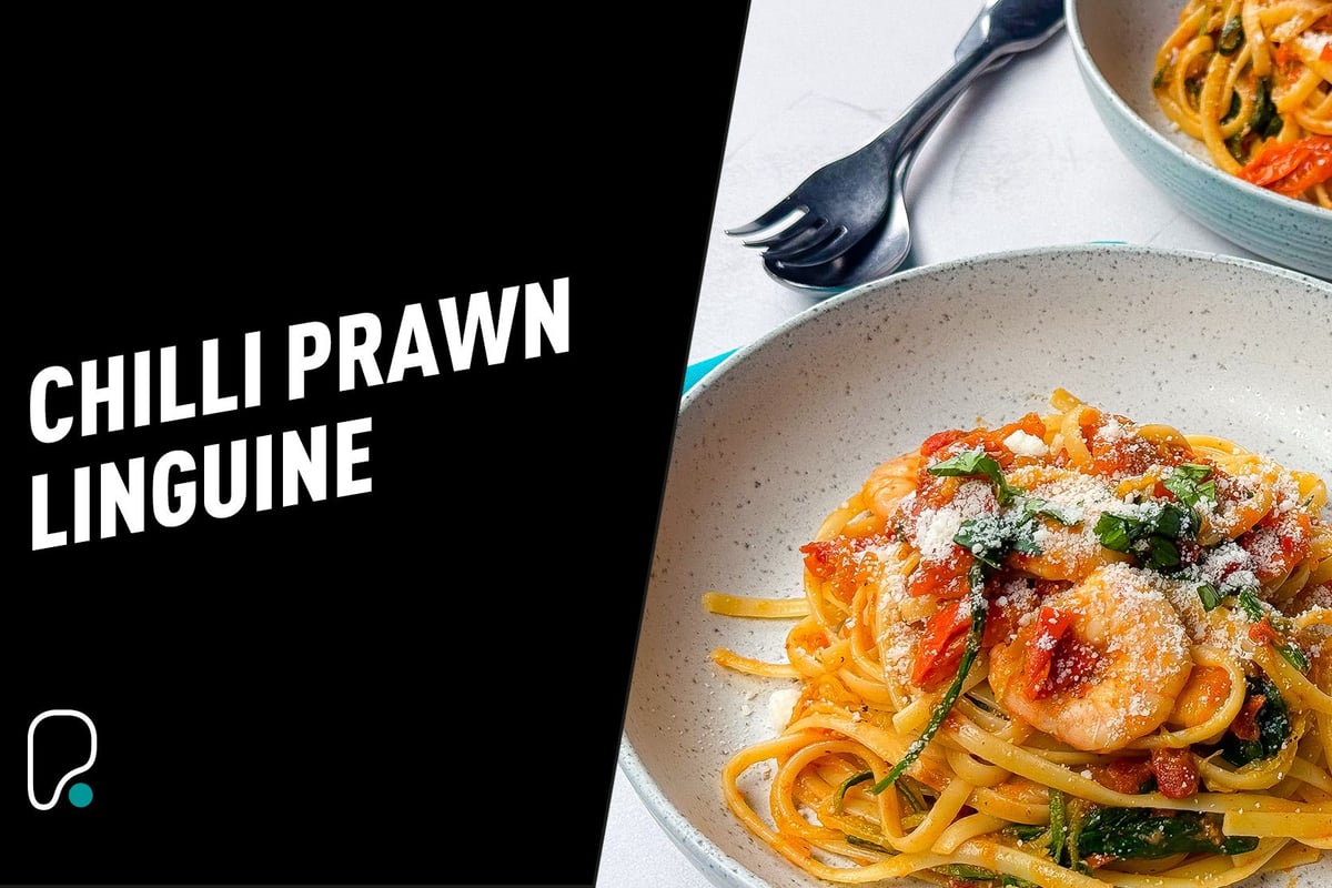 Chilli prawn linguine with grated cheese and herbs served in a bowl with cutlery nearby