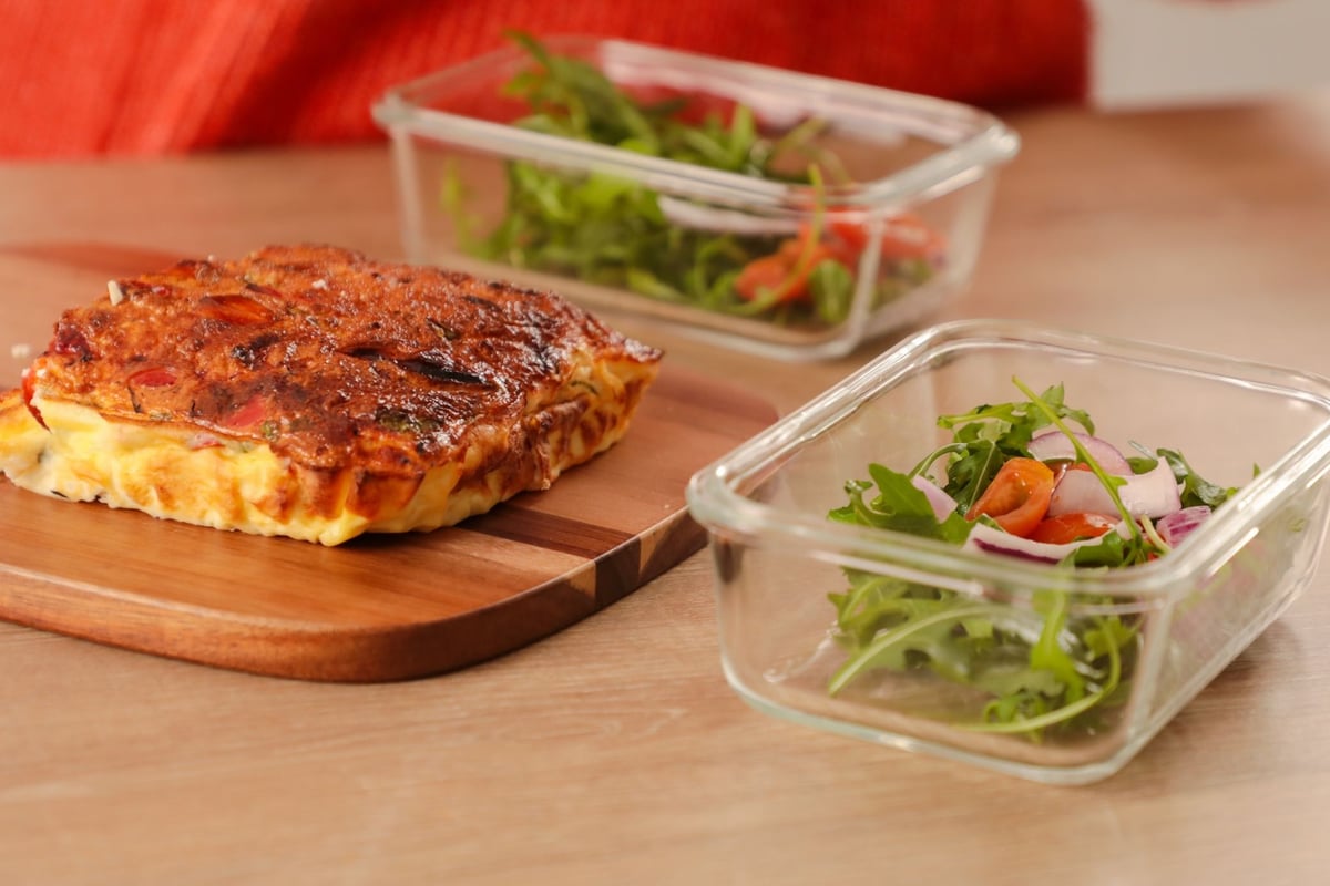 Sweet potato frittata on wooden board with two containers of fresh green salad