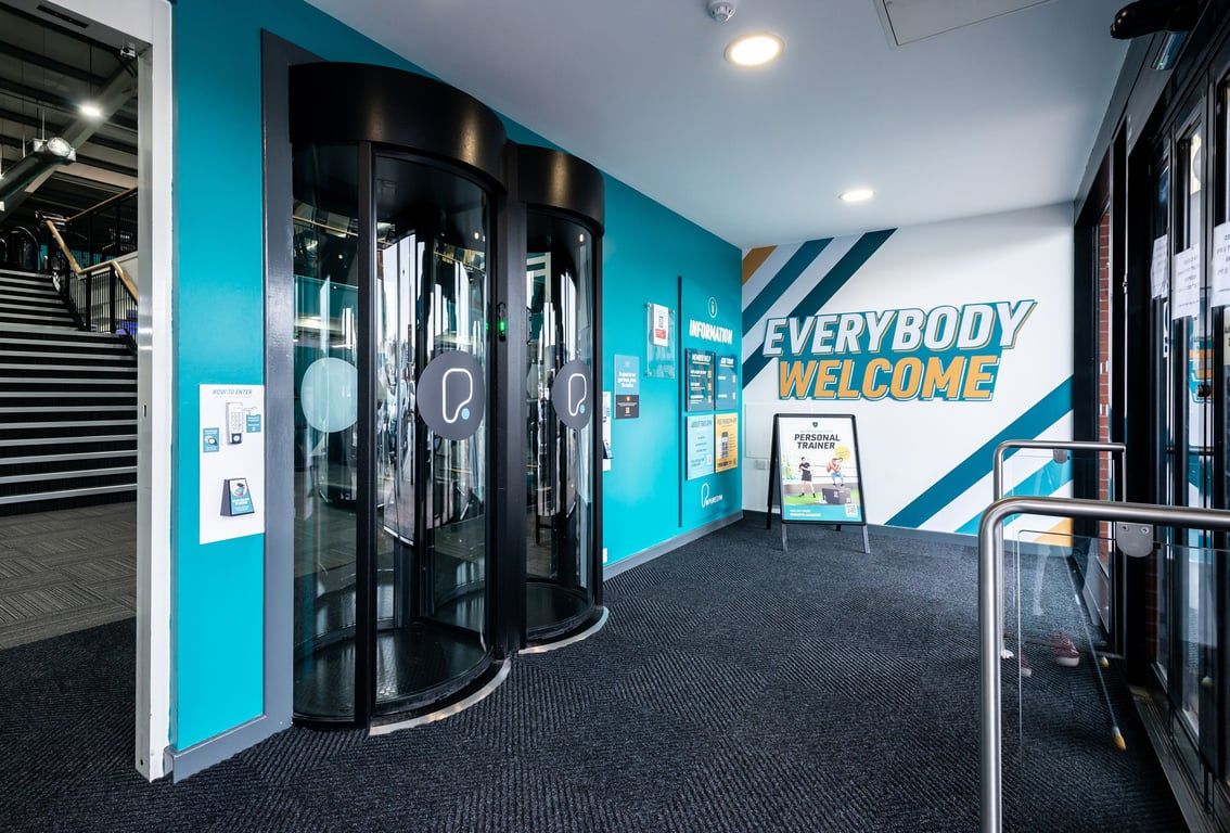 PureGym Wrexham: Rows of exercise machines, entry turnstiles, and a vibrant colour scheme welcoming guests.