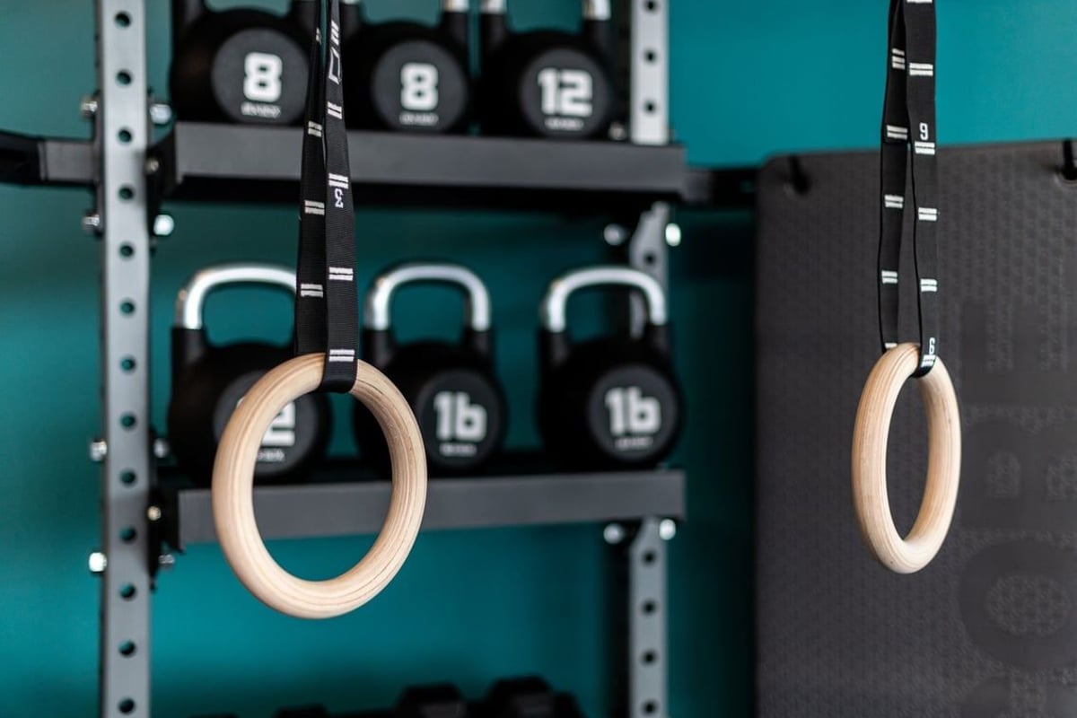 PureGym Yate: Wooden gymnastic rings hanging from racks alongside kettlebells and weight plates.