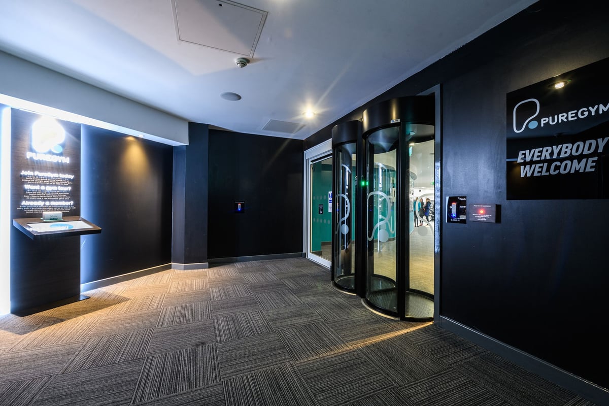 PureGym Aylesbury: Modern gym lobby with dark tones, glass doors, and illuminated signage.