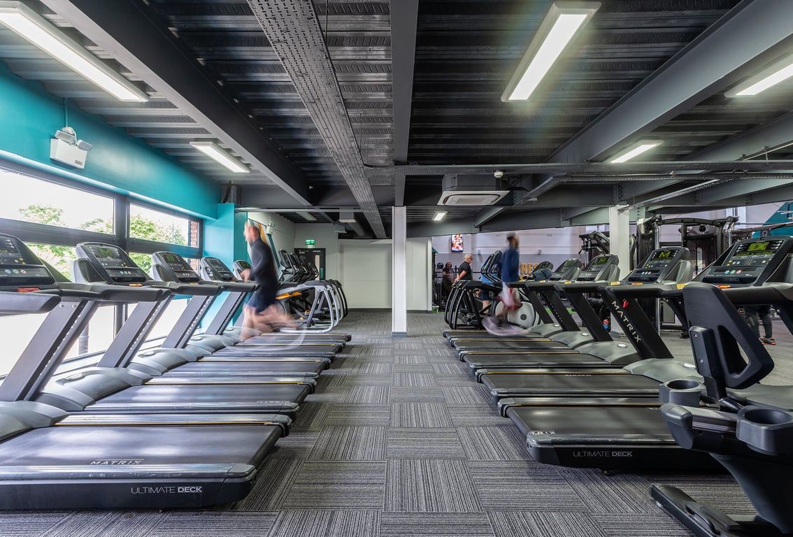 PureGym Aintree: Rows of treadmills, ellipticals, and other cardio machines in a gym setting with teal accents.