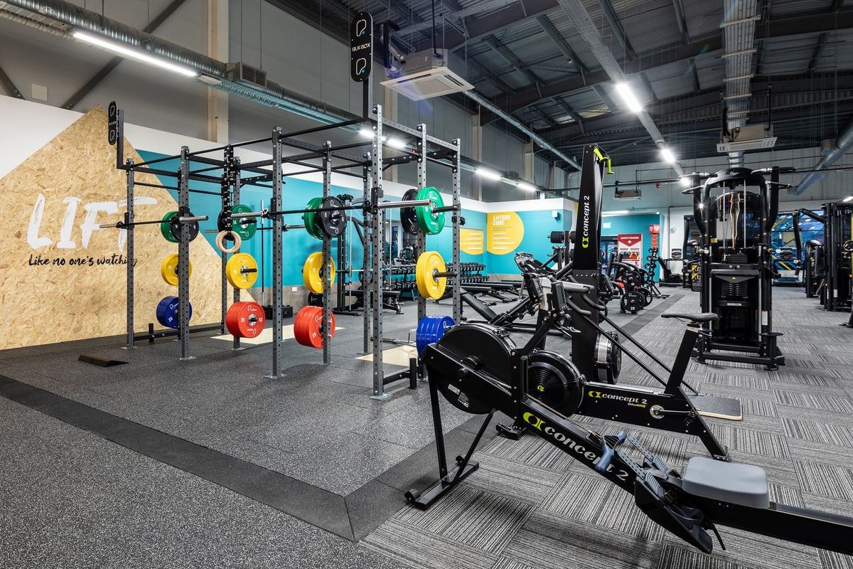 PureGym Wantage: Crisscrossed squat racks, weight plates in multiple colours, benches, and rubberized flooring.