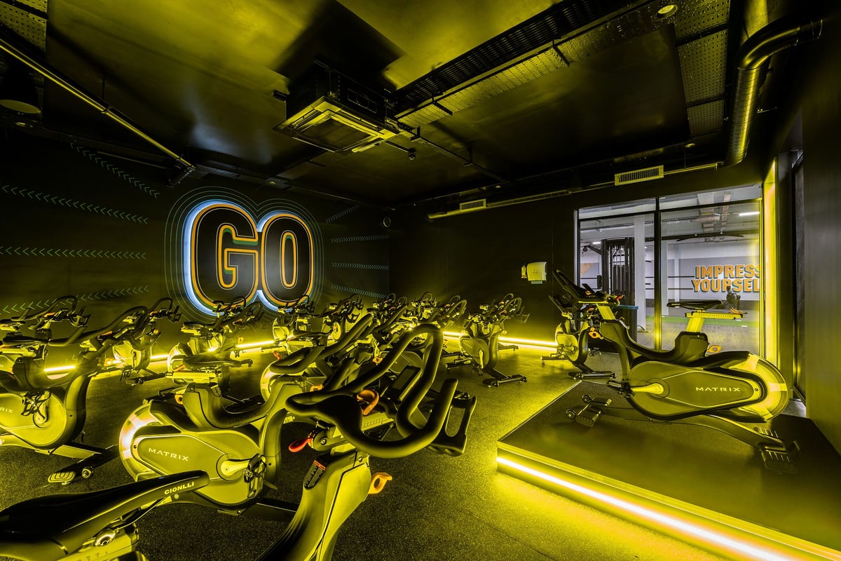 PureGym Durham Arnison: Rows of stationary cycles with neon "GO" signage in a dimly lit studio.