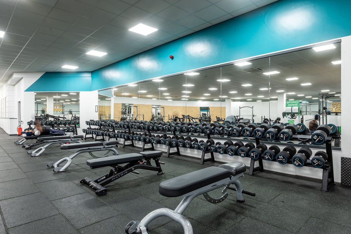 PureGym Birmingham Beaufort Park: Rows of weight benches, free weights, and exercise machines in a brightly lit gym interior.