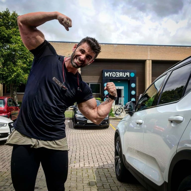 muscular man flexing arms in front of gym building and parked cars on cloudy day