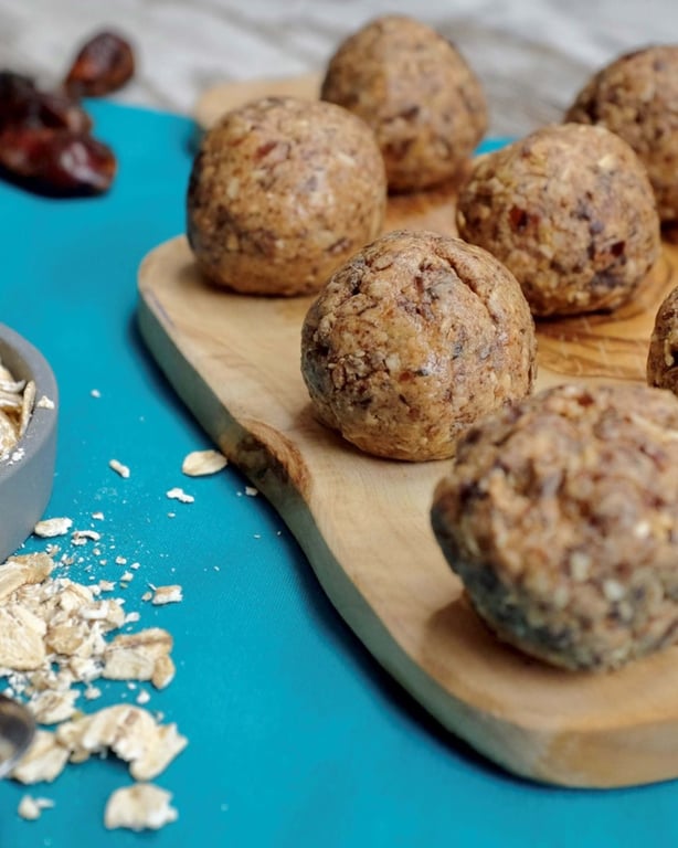 Energy balls on a wooden board with oats and dates on a blue surface nearby