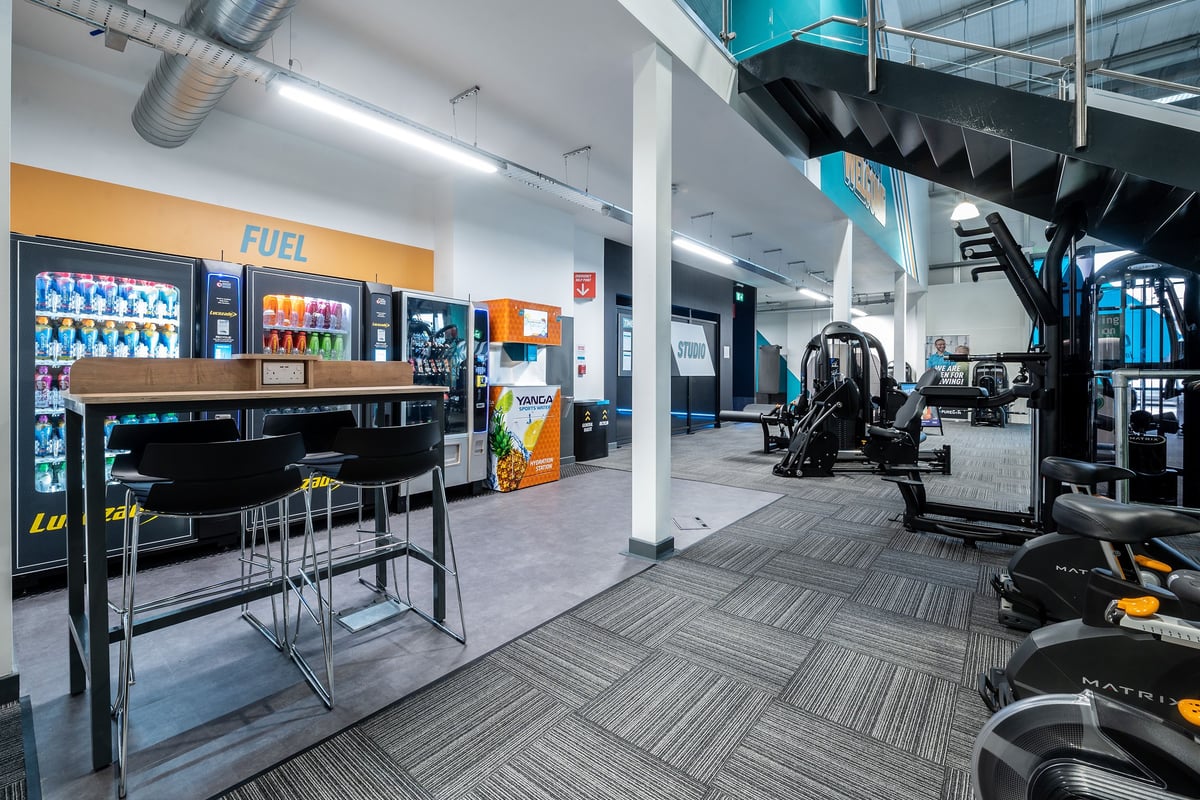 PureGym Cirencester: Fuel bar, seating area, workout machines, and rubberized flooring in a gym setting.