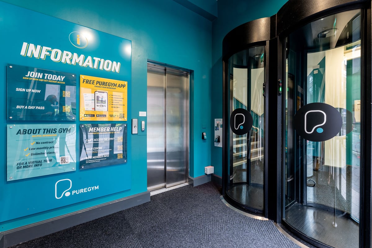 PureGym Newcastle Eldon Garden: An entrance area with information posters, glass doors, and a teal color scheme.