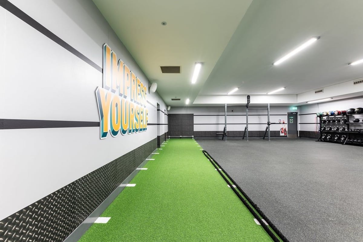 PureGym Cambridge Leisure Park: Turf track, weight racks, rubberized flooring, vibrant interior with motivational wall graphics.