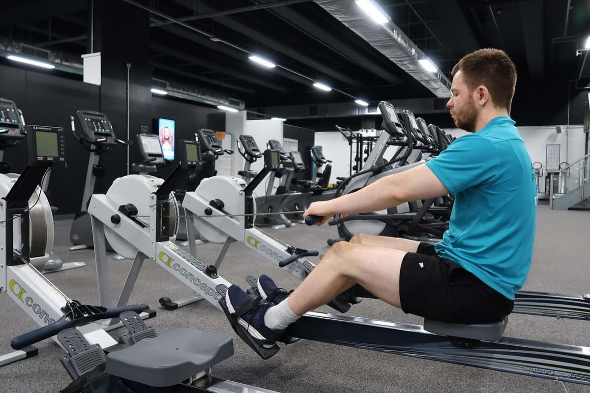 Man in blue shirt using rowing machine in gym with exercise bikes in background