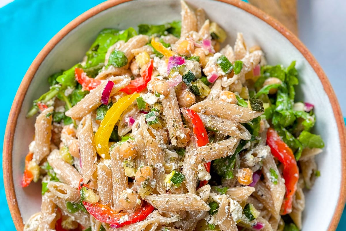 Bowl of whole wheat penne pasta salad with chickpeas, red and yellow peppers, and herbs.