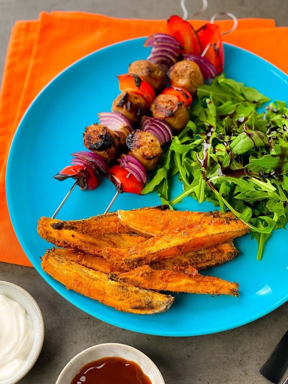 Grilled vegetable skewers with sweet potato fries and salad on a blue plate.