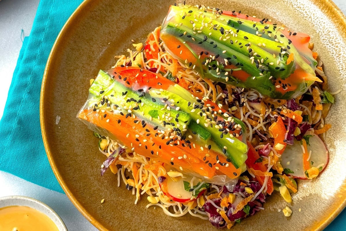 Two vegetable spring rolls with sesame seeds on a bed of salad in a brown bowl