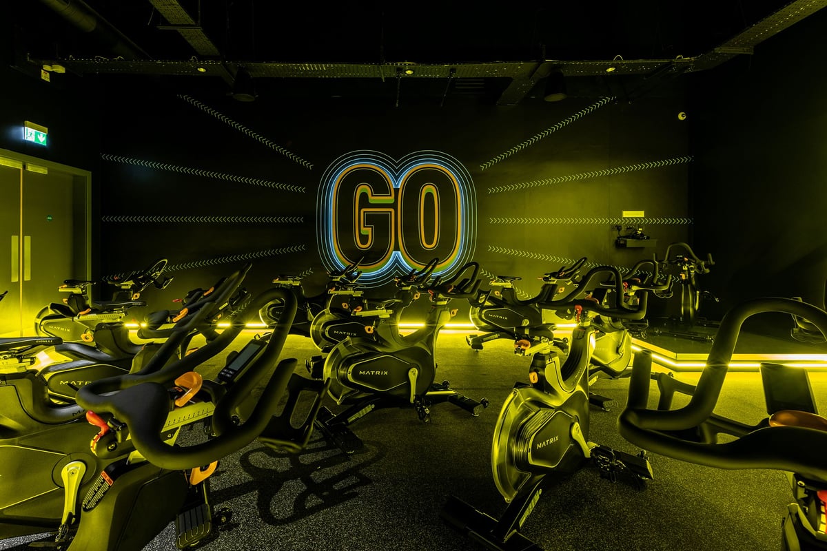 PureGym Sheffield Meadowhall Retail Park: Rows of spin bikes illuminated by neon "GO" signage in a dark exercise studio.