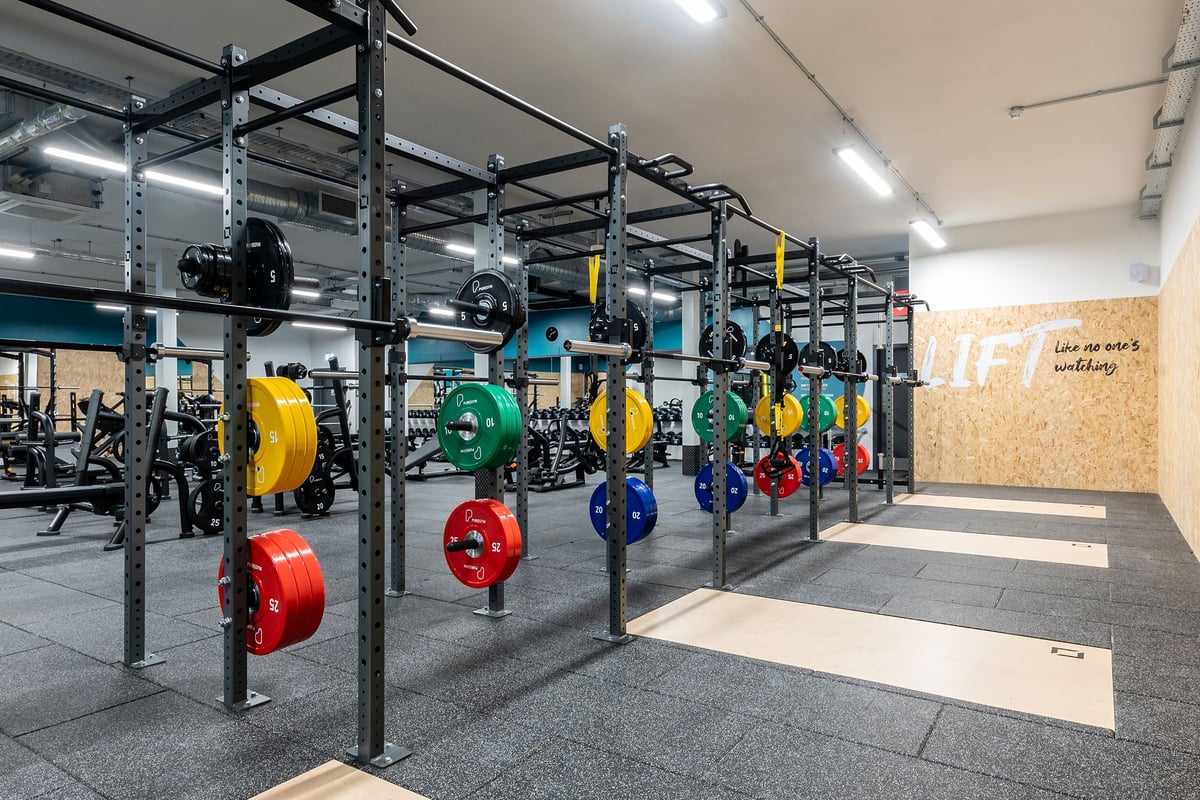 PureGym Kettering: Squat racks, weight plates in various colours, rubberized flooring in a gym setting.