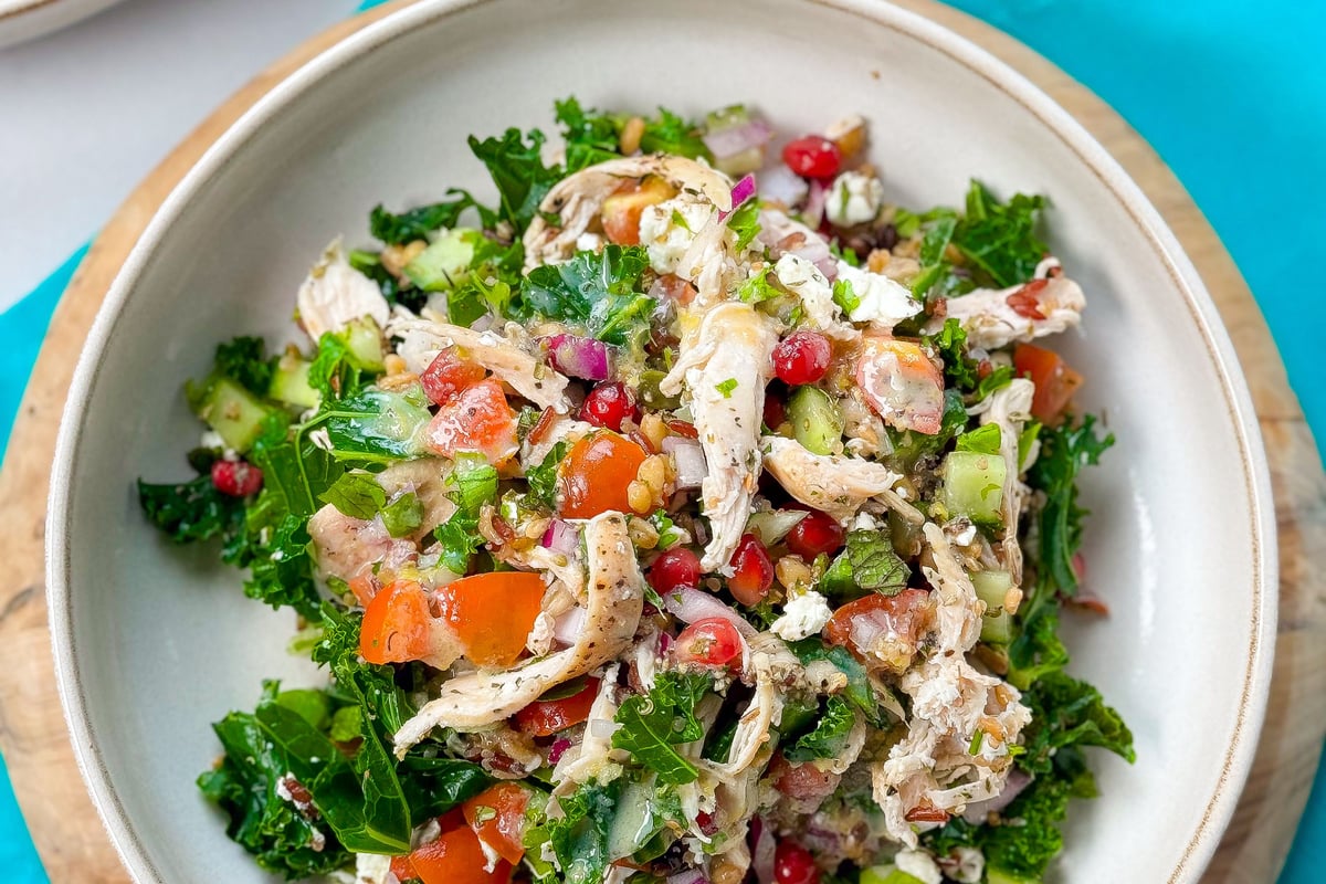 Bowl of mixed salad with shredded chicken, kale, tomatoes, cucumber, and pomegranate seeds