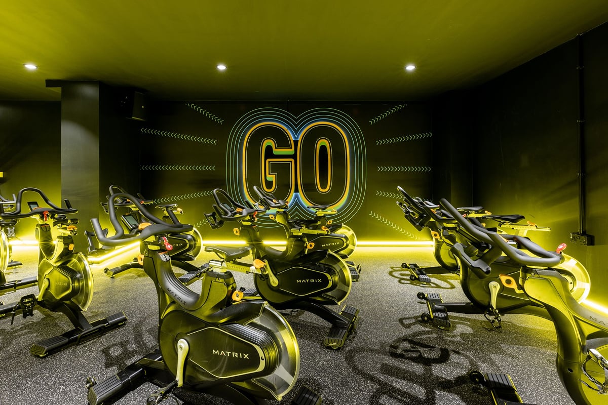 PureGym London Finsbury Park: Rows of exercise bikes in a dimly lit studio with neon "GO" signage on the wall.