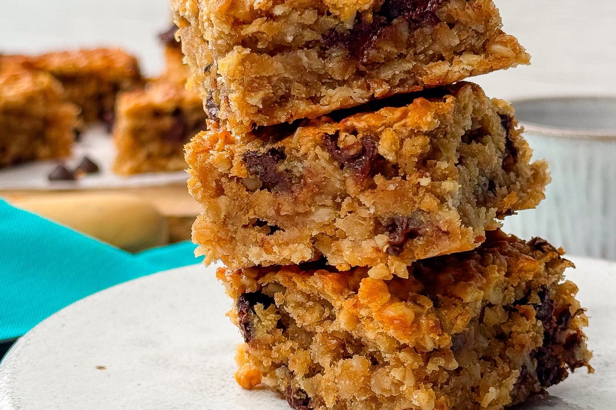 Stack of three chocolate chip oat bars on a white plate with a teal cloth underneath