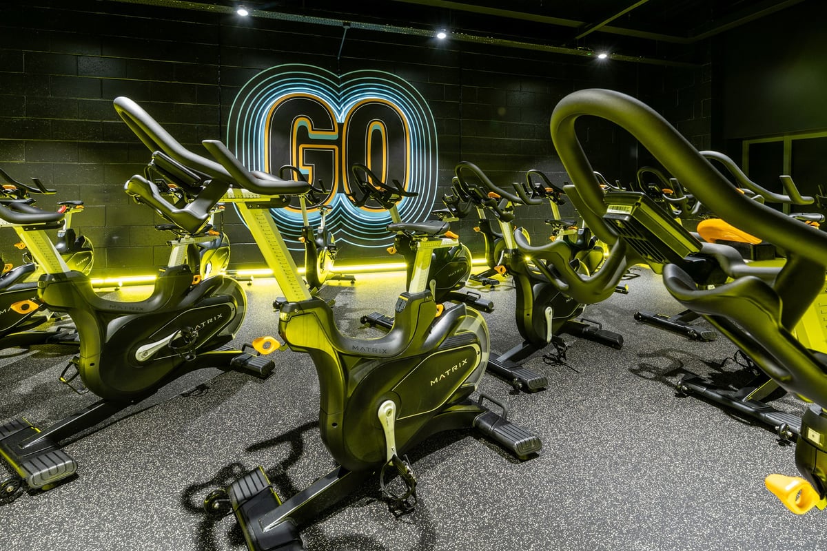 PureGym London Orpington Central: Spin bikes, neon signage, and dimly lit studio interior with rubberized flooring.