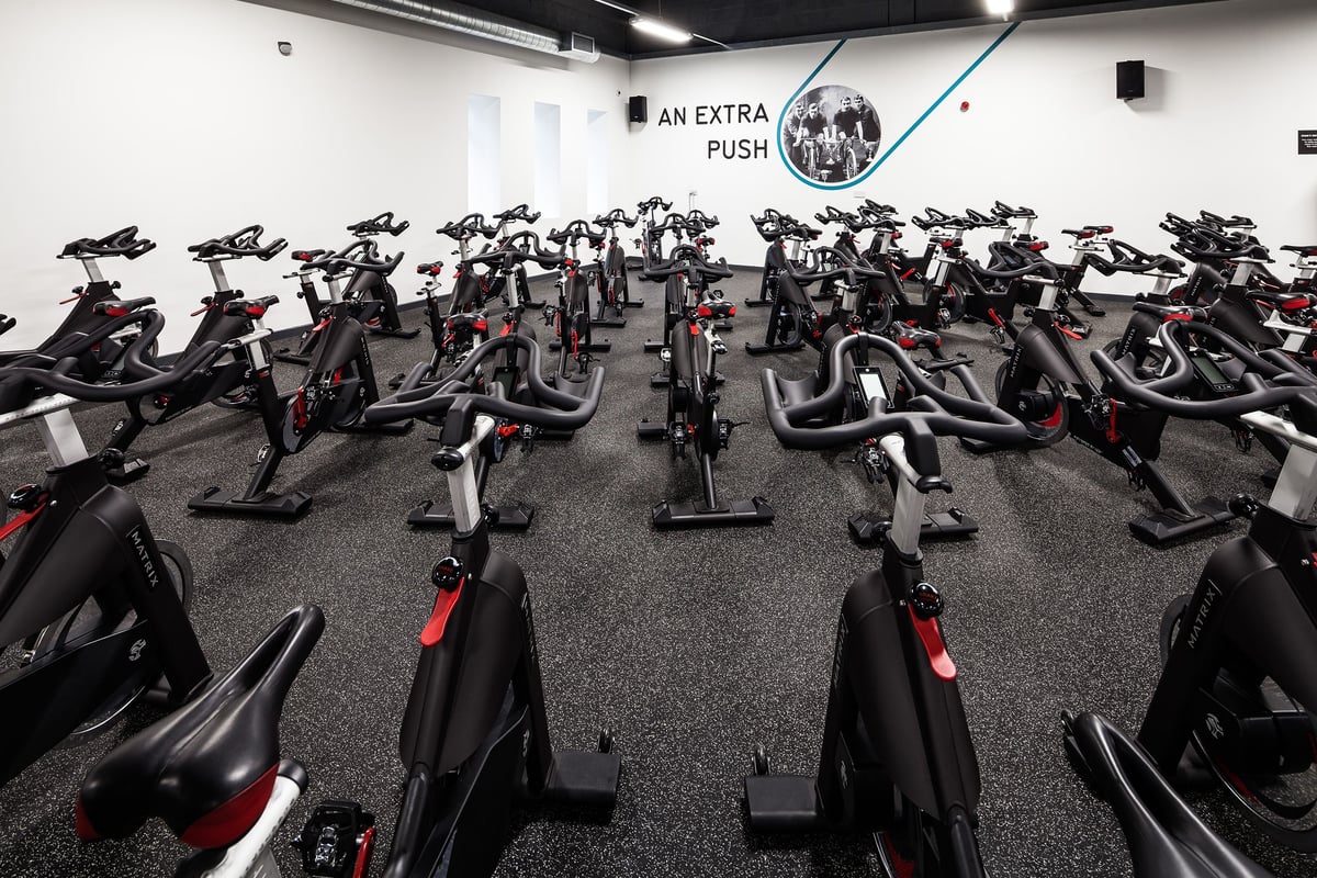 PureGym Manchester Stretford: Rows of stationary bikes in a dimly lit studio with motivational slogan on the wall.