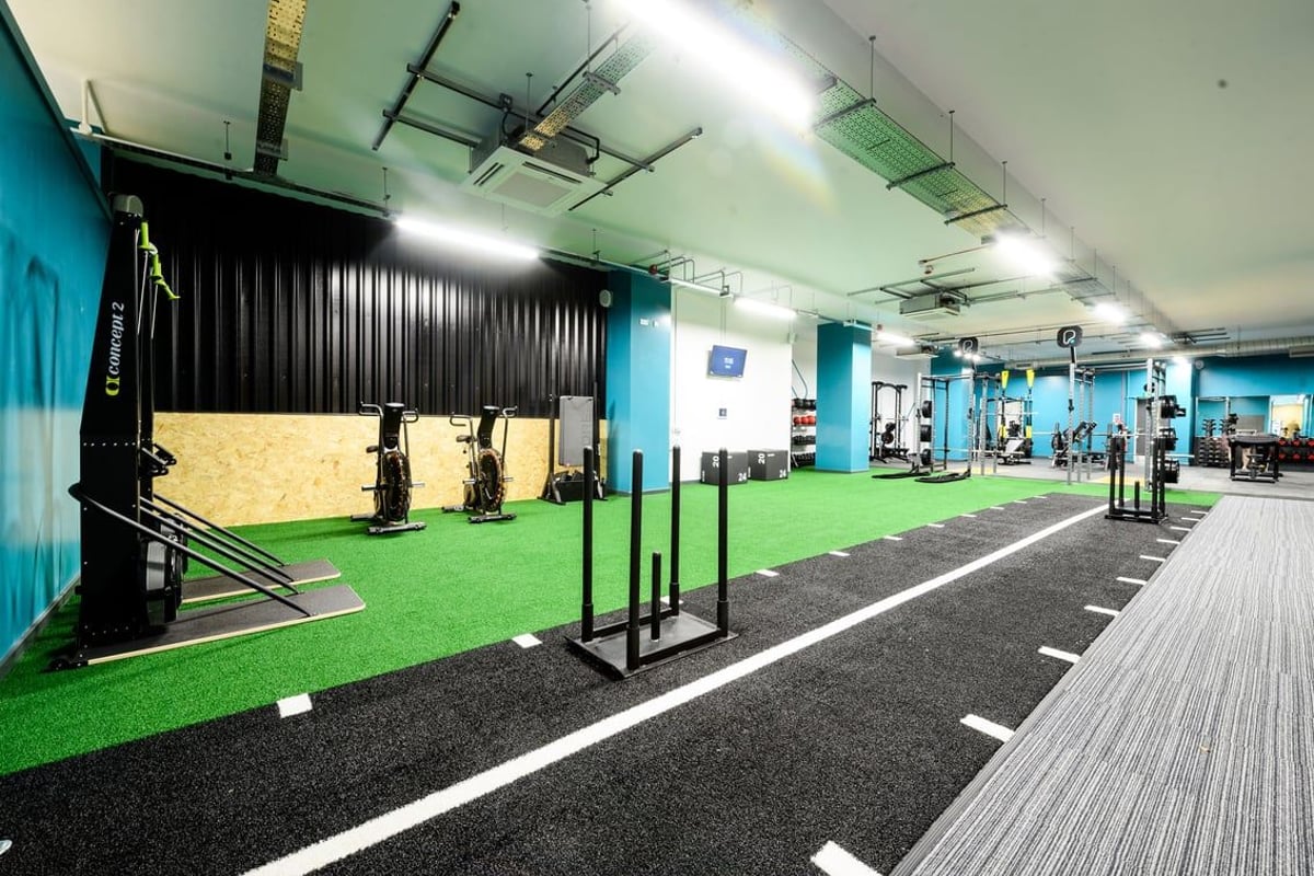 PureGym East Grinstead: Indoor gym area with putting green, lifting racks, weight plates, and rubberized floor.