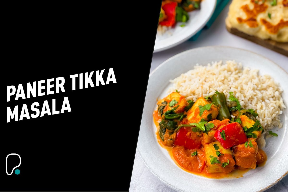 Plate of paneer tikka masala with rice and naan bread in the background