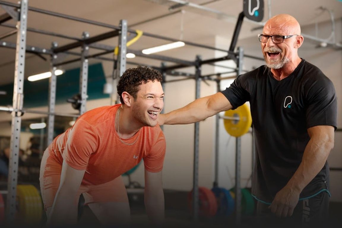 A PureGym member working out with a smiling personal trainer