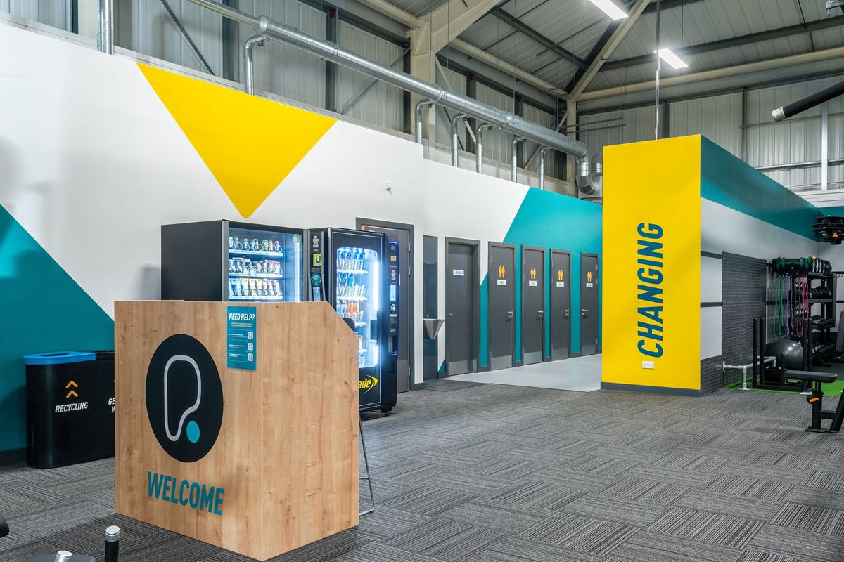 PureGym Oswestry: Vending machines, welcome signage, and a teal and yellow branded gym entrance space.