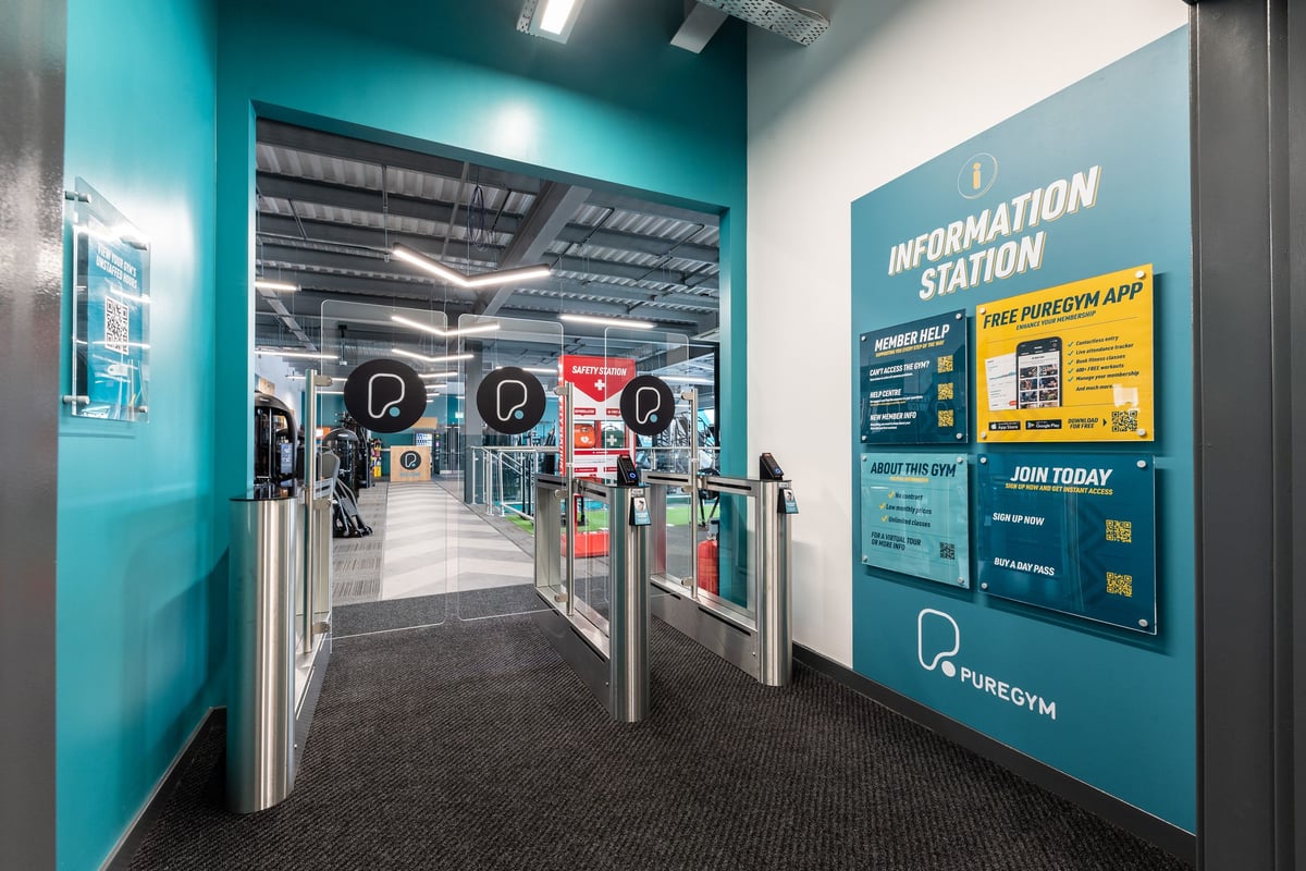 PureGym Yate: Entry turnstiles, information kiosk promoting gym membership, and tiled walkway.