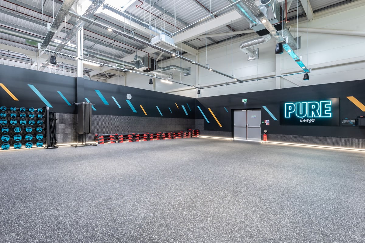 PureGym Nottingham Colwick: Spacious gym with colourful accent walls, rows of weight plates, and rubberized flooring.