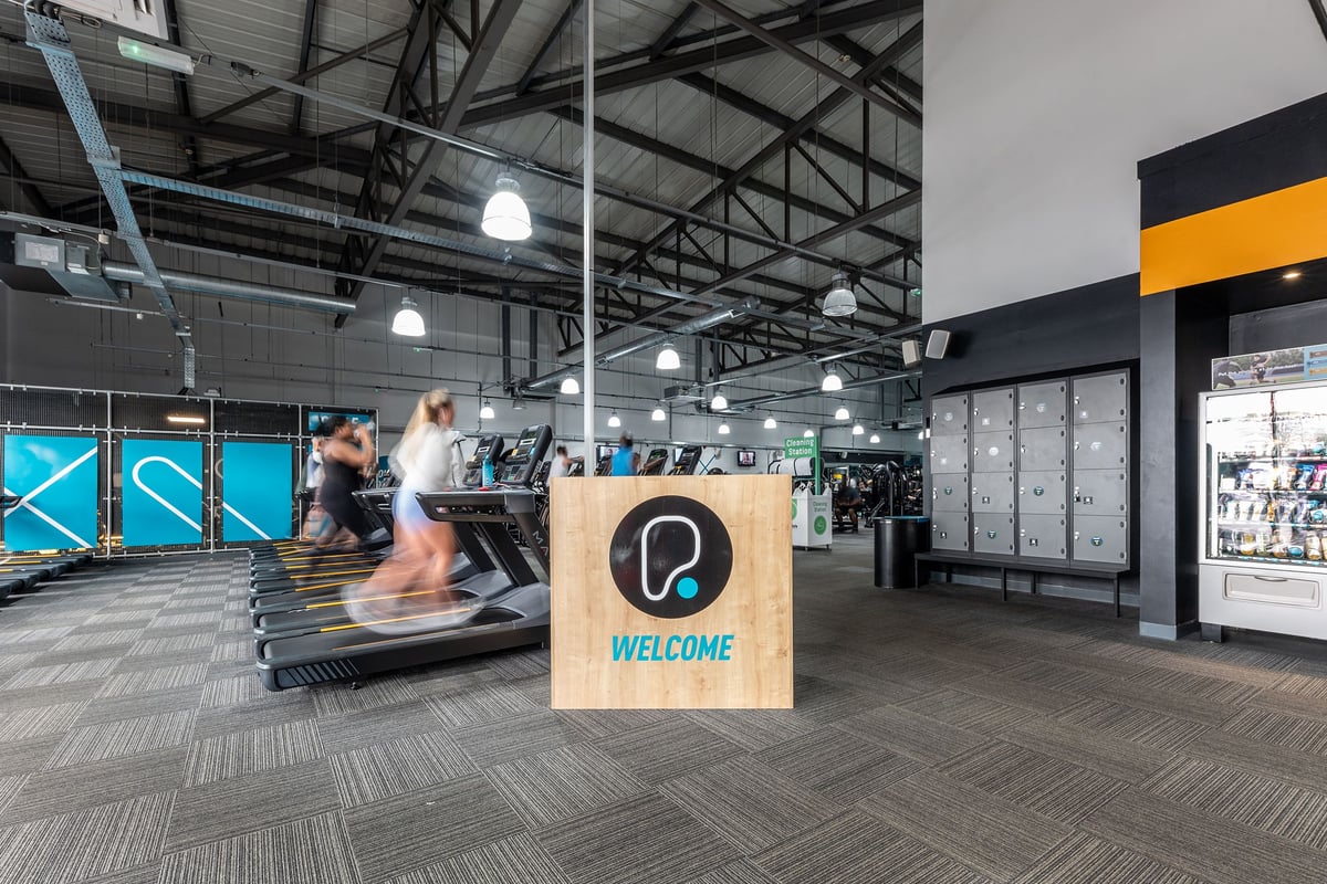 PureGym Wolverhampton Bentley Bridge: Cardio machines, welcome sign, merchandise displays, open layout with high ceilings.