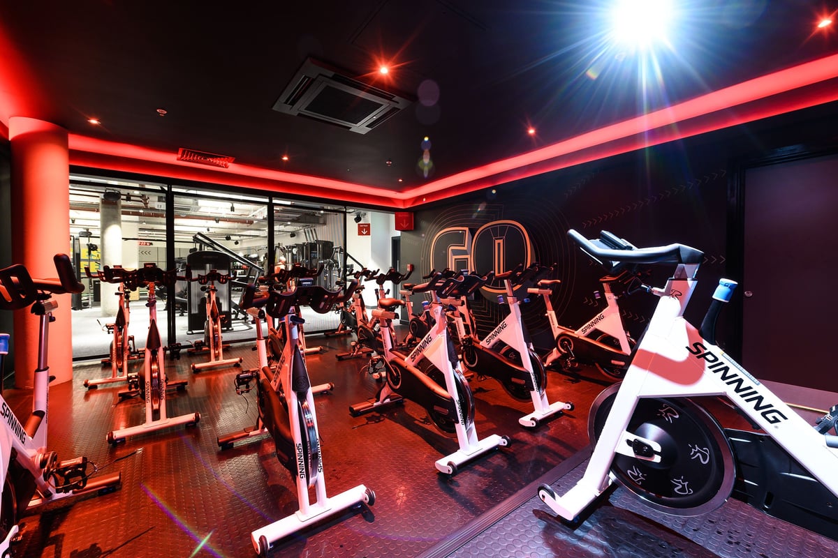 PureGym London Fulham: Rows of stationary bikes, treadmills, weight machines in a neon-lit fitness studio.