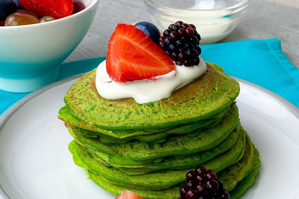 Stack of green pancakes topped with cream, strawberries, blackberries, and blueberries on
