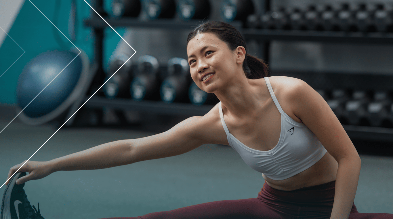 A woman performs a stretching exercise in a gym, focusing on flexibility and fitness.