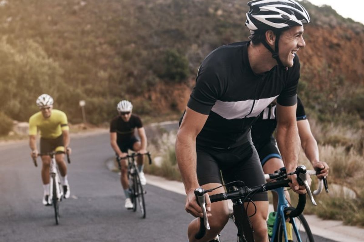 Drei Radfahrer fahren auf einer Bergstraße mit hügeliger Landschaft im Hintergrund.