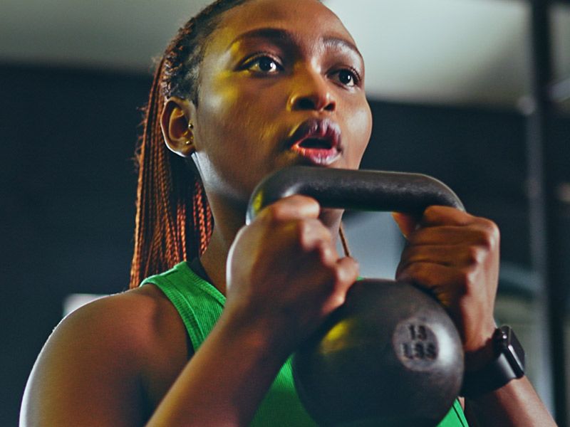 Frau im grünen Top hebt während des Trainings eine 15-Pfund-Kettlebell.