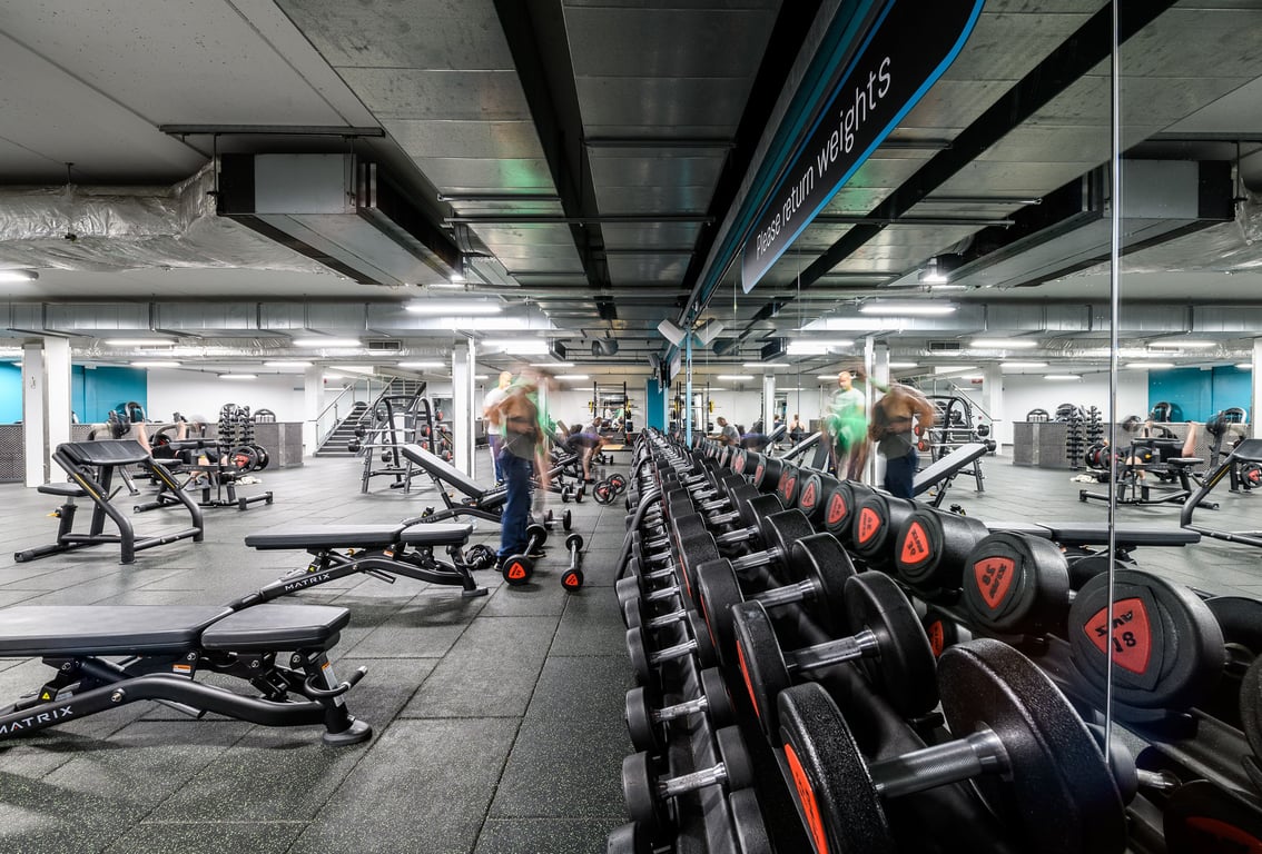 PureGym Manchester Urban Exchange: Weight racks, free weights, benches, mirrors, and equipment in a basement gym setting.