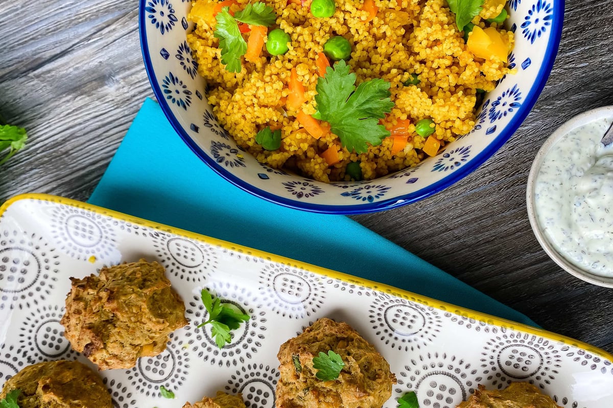 Bowl of spiced couscous with peas and carrots beside falafel and herb yoghurt