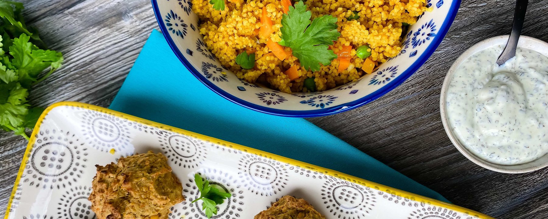 Bowl of spiced couscous with peas and carrots beside falafel and herb yoghurt