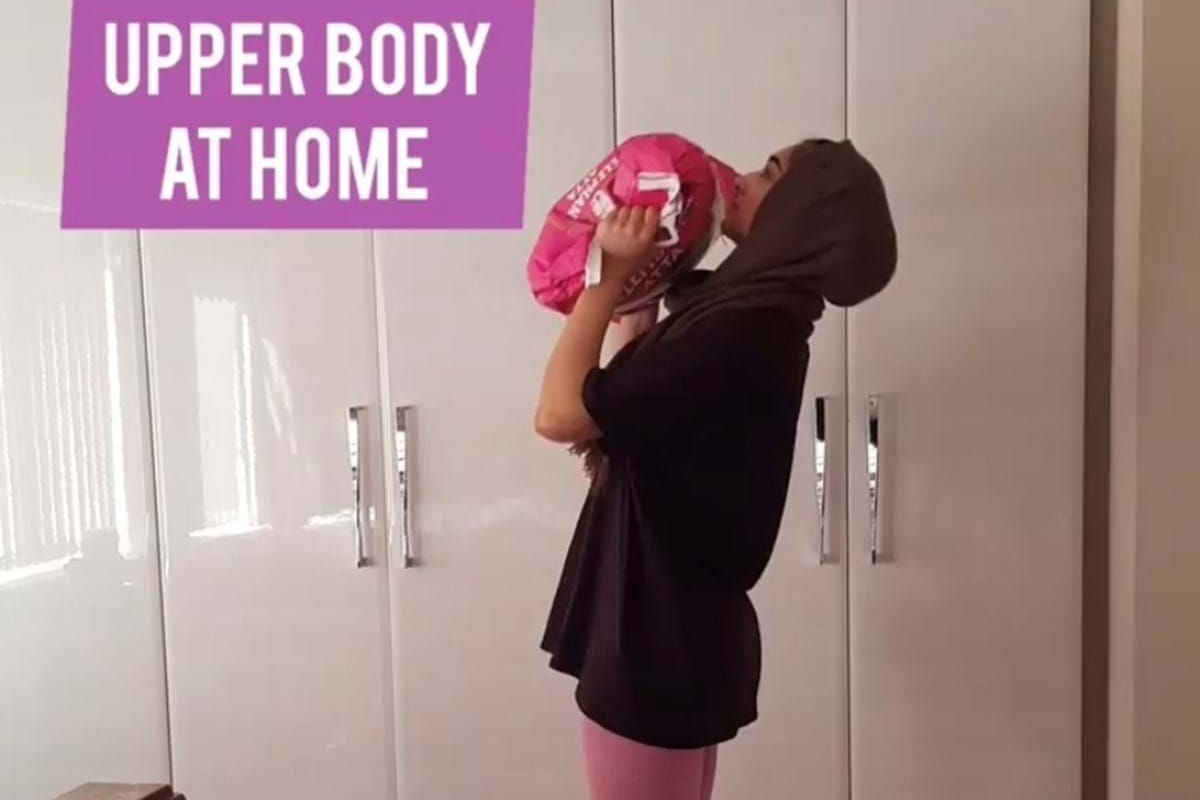 Woman in hijab lifting a pink bag on a purple mat in a bedroom with white wardrobes