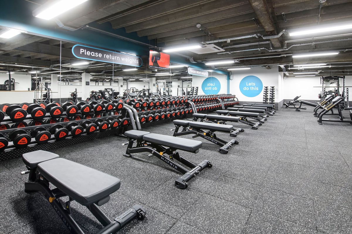 PureGym Brighton London Road: Free weight benches, dumbbell racks and weight plates in a weightlifting area.