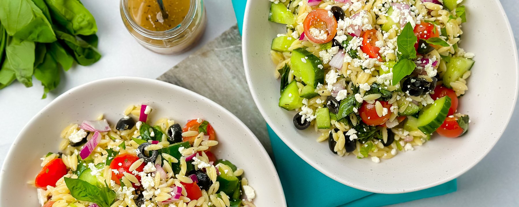 Two white bowls of orzo pasta salad with cucumber, tomatoes, olives and feta