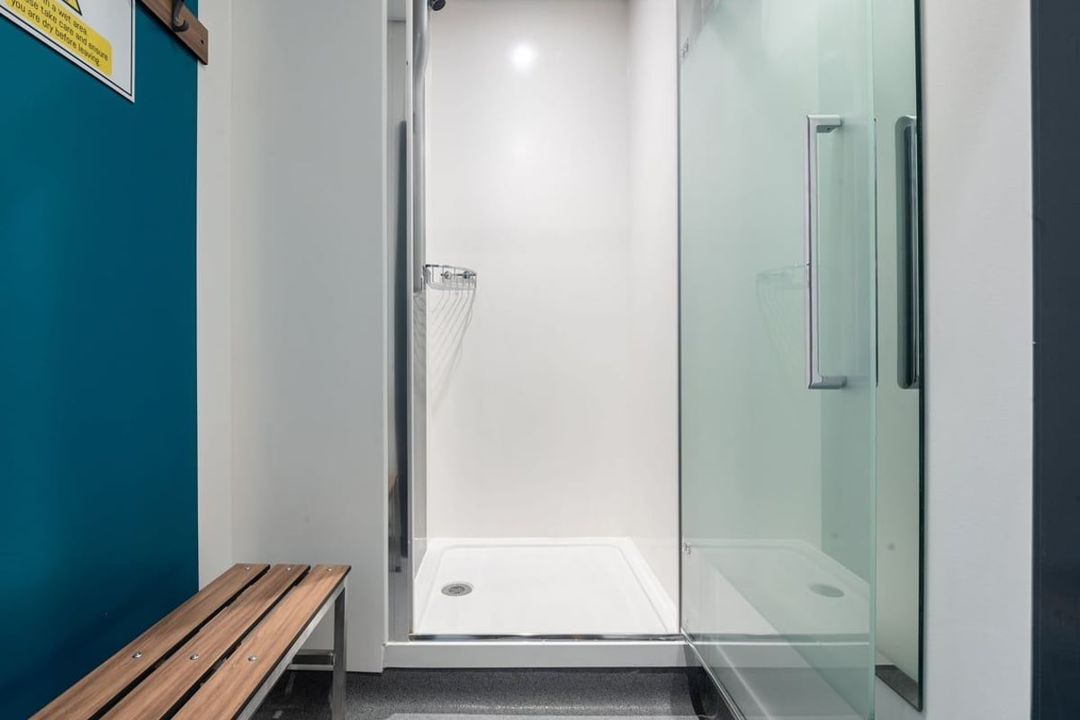 PureGym Lanark: Shower area with tiled walls, glass enclosure, wooden bench.