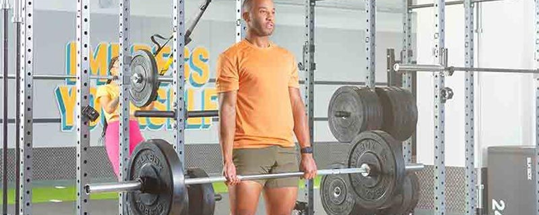 Homme en t-shirt orange soulevant une barre avec poids dans une salle de sport.