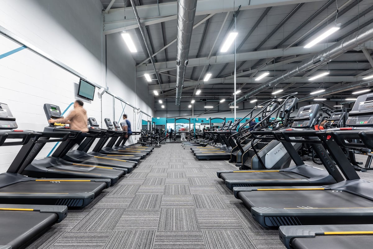 PureGym Birmingham West: Rows of treadmills, brightly lit gym with exposed ceiling ducts and reinforced rubberised flooring.