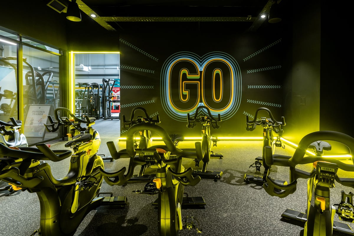PureGym Glasgow Rutherglen: Rows of stationary exercise bikes in bright yellow lighting with "GO" neon signage.