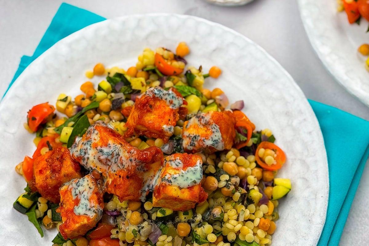 Spiced tofu pieces with herb dressing on colourful couscous salad with vegetables