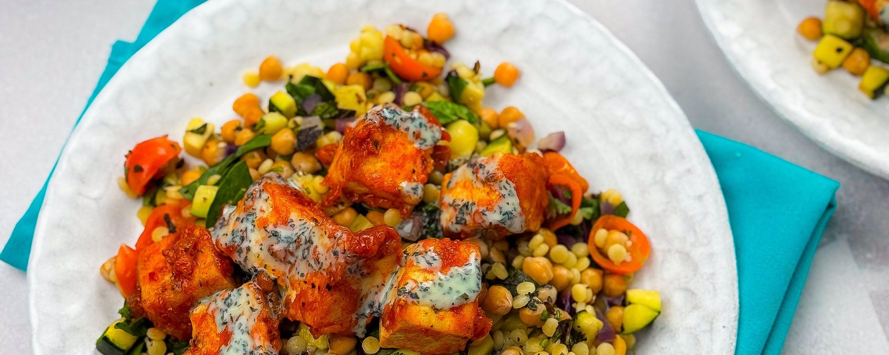 Spiced tofu pieces with herb dressing on colourful couscous salad with vegetables